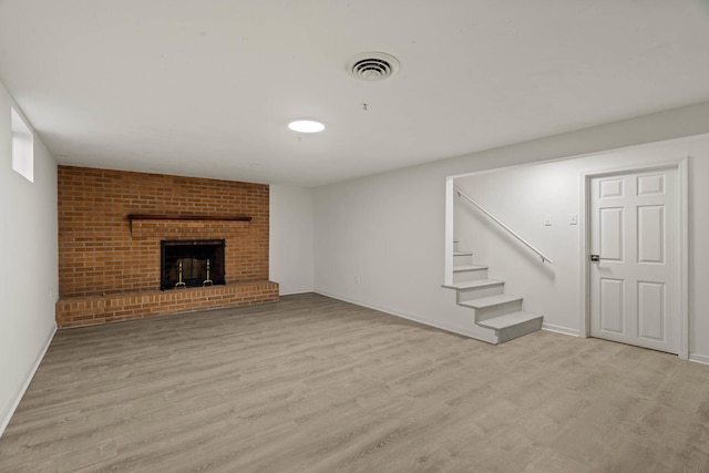 finished below grade area featuring baseboards, visible vents, stairs, light wood-type flooring, and a brick fireplace