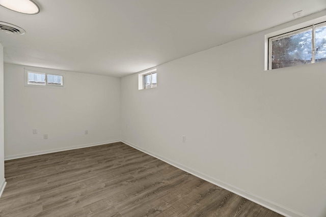 below grade area with dark wood finished floors, visible vents, and baseboards