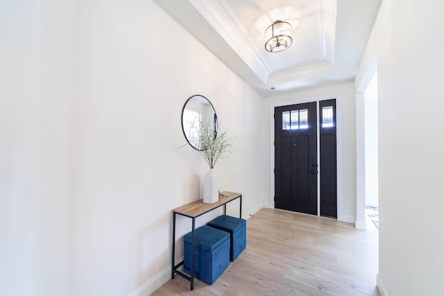 entryway featuring light wood-type flooring, baseboards, a raised ceiling, and crown molding