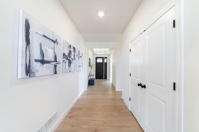 hall with light wood-type flooring, visible vents, and baseboards