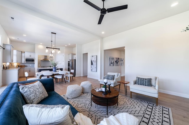 living room with ceiling fan with notable chandelier, light wood finished floors, visible vents, and baseboards