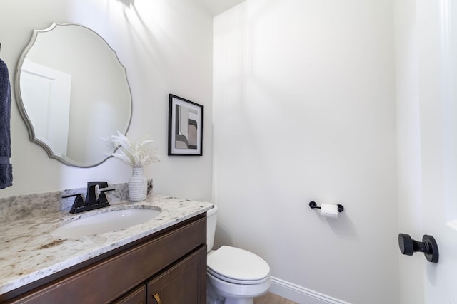 half bath featuring baseboards, vanity, and toilet