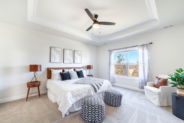 bedroom with ceiling fan, light colored carpet, visible vents, baseboards, and a tray ceiling