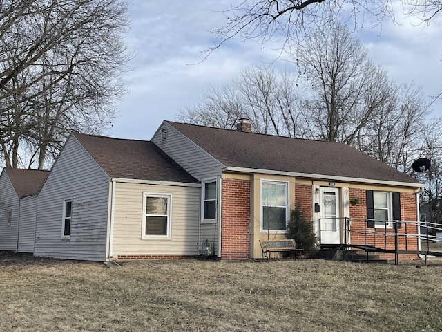 view of front of home featuring roof with shingles, a chimney, a front lawn, and brick siding