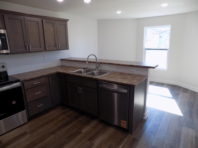 kitchen featuring stainless steel appliances, dark wood-type flooring, a sink, and a peninsula