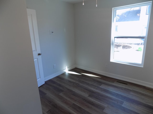 unfurnished room with dark wood-style floors, visible vents, and baseboards