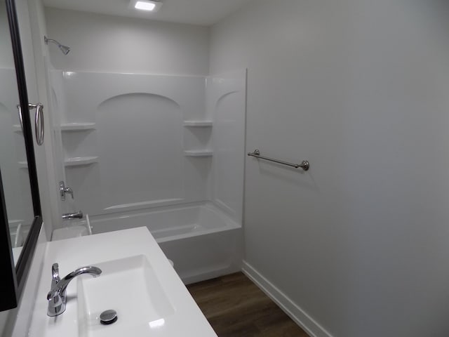 full bath with baseboards, wood finished floors, a sink, and shower / bathing tub combination