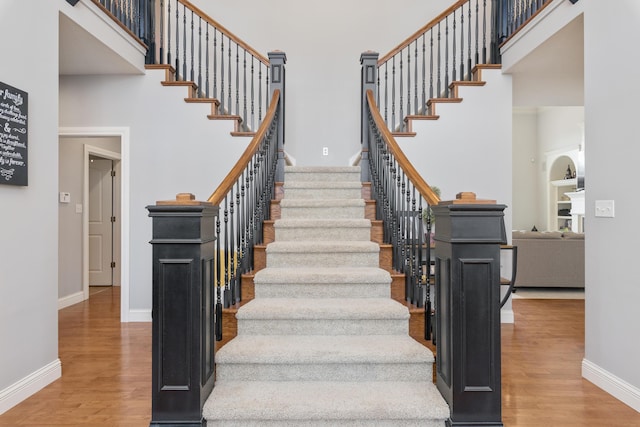 stairway featuring a towering ceiling, baseboards, and wood finished floors