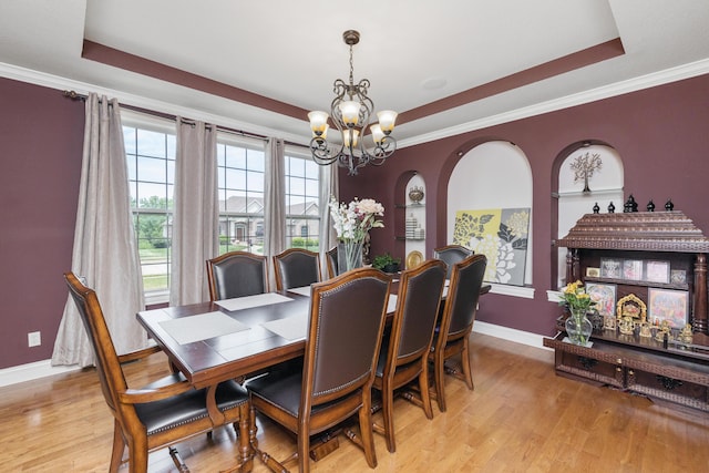 dining area featuring a tray ceiling, baseboards, a notable chandelier, and light wood finished floors