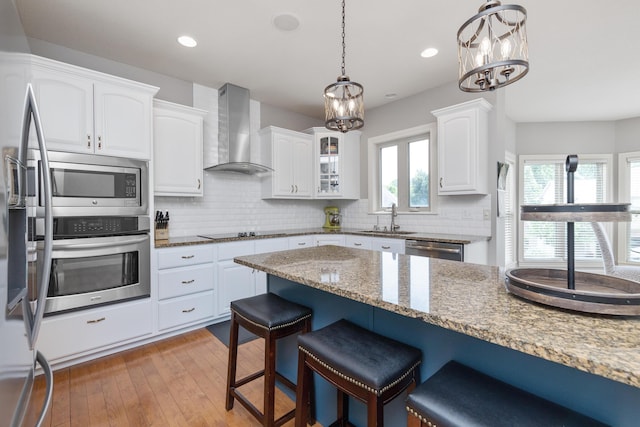 kitchen featuring wall chimney exhaust hood, a breakfast bar area, white cabinetry, and stainless steel appliances