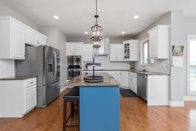 kitchen with stainless steel appliances, a kitchen island, a sink, wall chimney exhaust hood, and wood-type flooring