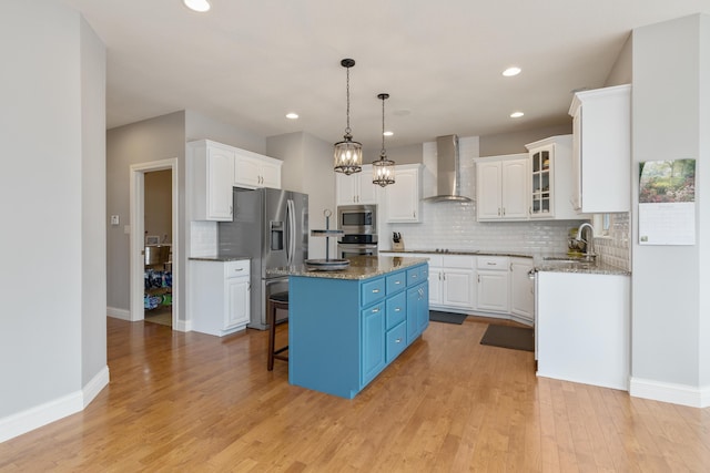 kitchen with a center island, appliances with stainless steel finishes, white cabinets, a sink, and wall chimney exhaust hood