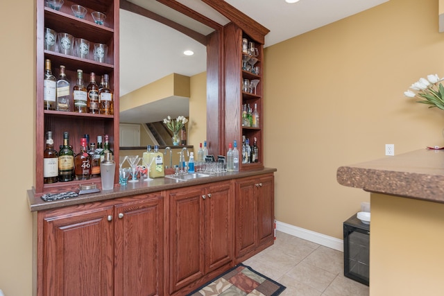 bar featuring a bar, light tile patterned floors, baseboards, and a sink