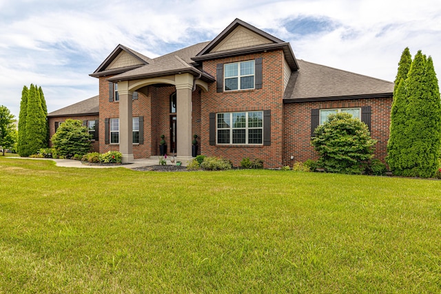 view of front of home featuring a shingled roof, a front yard, and brick siding