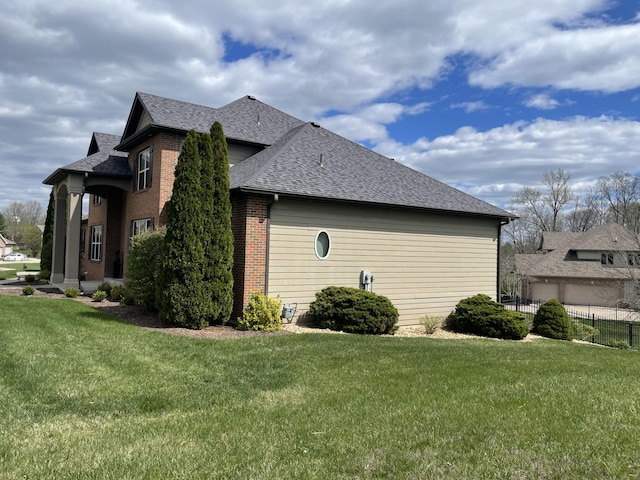 view of property exterior featuring roof with shingles, a lawn, brick siding, and fence