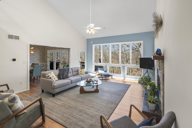 living area featuring high vaulted ceiling, a fireplace, wood finished floors, visible vents, and a ceiling fan