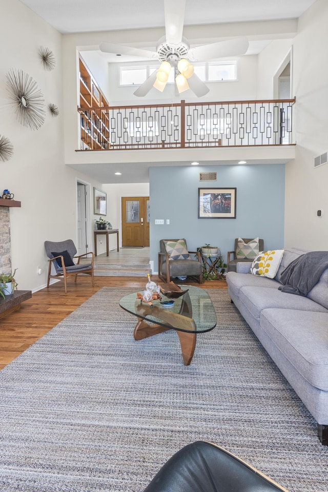 living room with baseboards, visible vents, a towering ceiling, ceiling fan, and wood finished floors