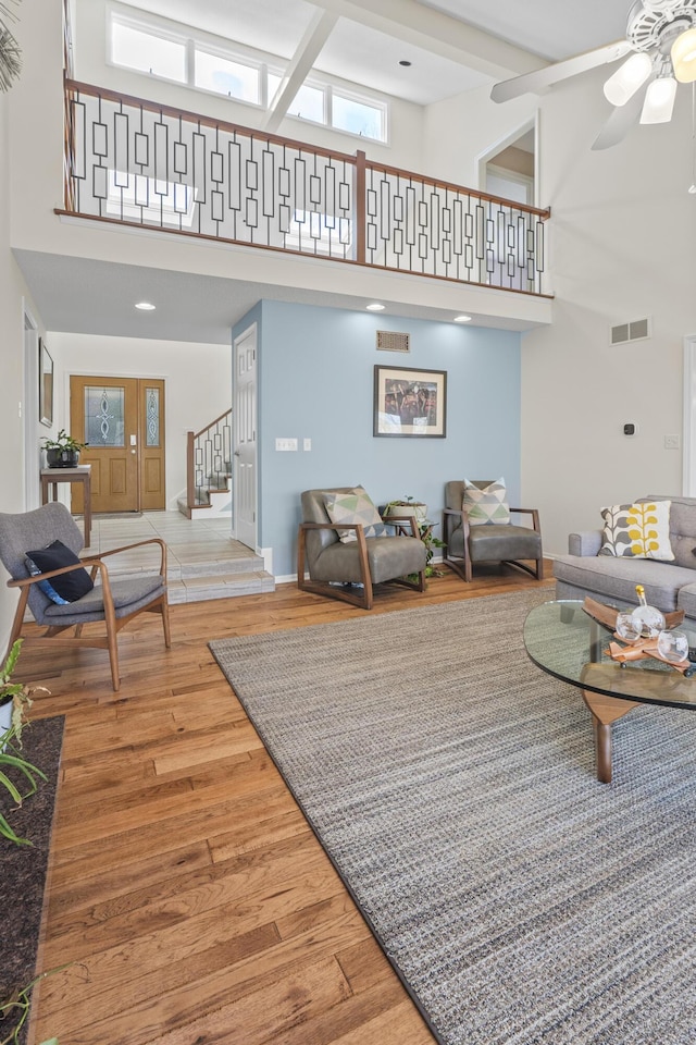 living area featuring visible vents, a ceiling fan, a towering ceiling, wood finished floors, and stairs