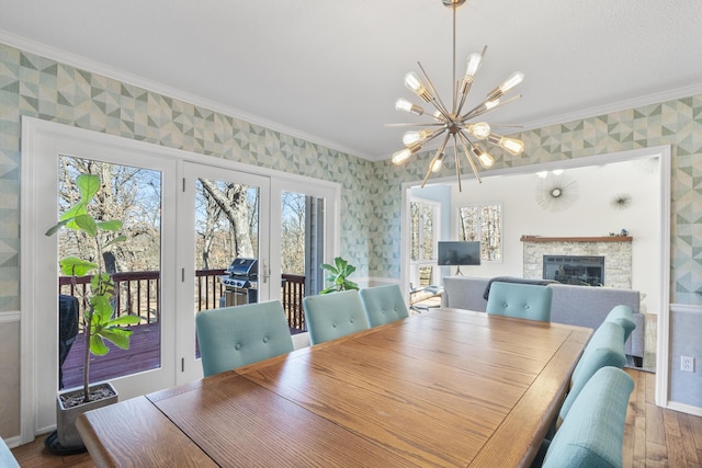 dining area with a tiled fireplace, crown molding, an inviting chandelier, and wallpapered walls