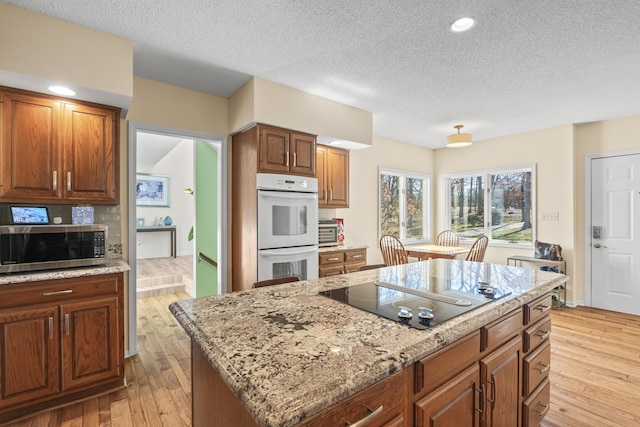 kitchen featuring double oven, black electric cooktop, light wood-type flooring, light stone countertops, and stainless steel microwave