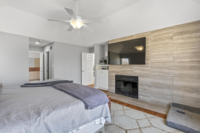 bedroom featuring ensuite bath, a tile fireplace, wood finished floors, and a ceiling fan