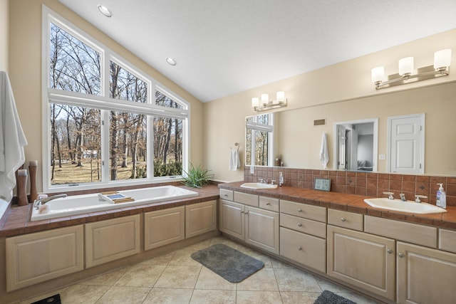 full bath featuring vaulted ceiling, tile patterned flooring, a sink, and a garden tub