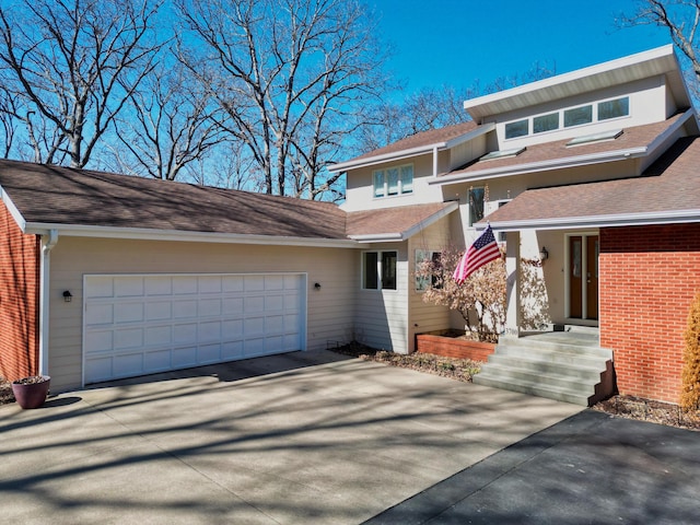 view of front facade with an attached garage, driveway, a shingled roof, and brick siding