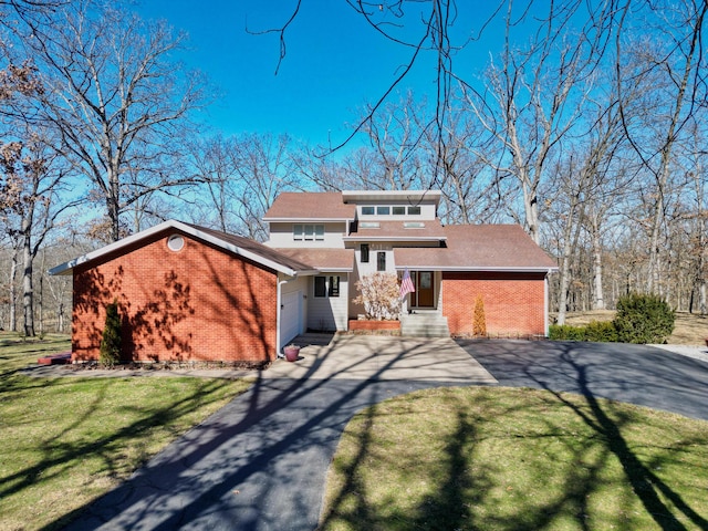 view of front of house with an attached garage, aphalt driveway, a front yard, and brick siding