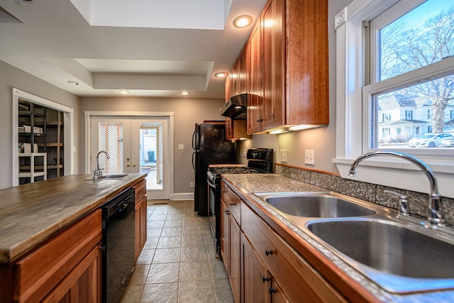 kitchen featuring black appliances, a tray ceiling, brown cabinetry, and a sink