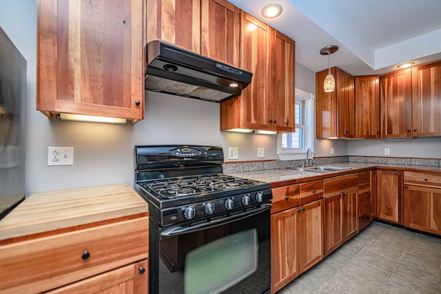 kitchen with brown cabinets, under cabinet range hood, pendant lighting, a sink, and gas stove