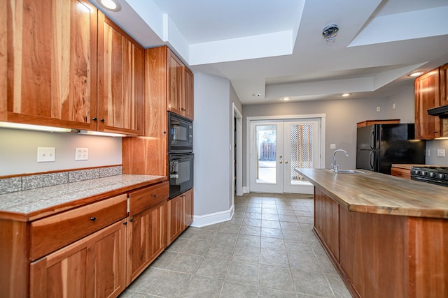 kitchen featuring a raised ceiling, butcher block counters, french doors, black appliances, and a sink