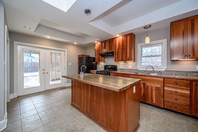 kitchen with under cabinet range hood, a sink, freestanding refrigerator, a tray ceiling, and range with gas cooktop