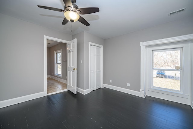 unfurnished room featuring dark wood-type flooring, visible vents, ceiling fan, and baseboards