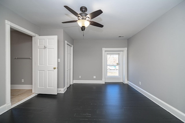 unfurnished room featuring dark wood-style floors, visible vents, baseboards, and a ceiling fan