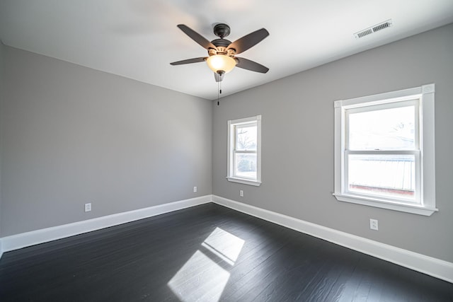 spare room with dark wood-style floors, baseboards, visible vents, and a ceiling fan