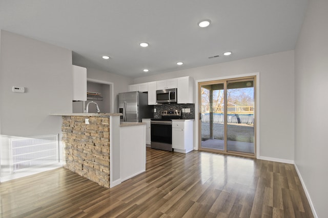 kitchen with backsplash, appliances with stainless steel finishes, dark wood-type flooring, white cabinetry, and a peninsula