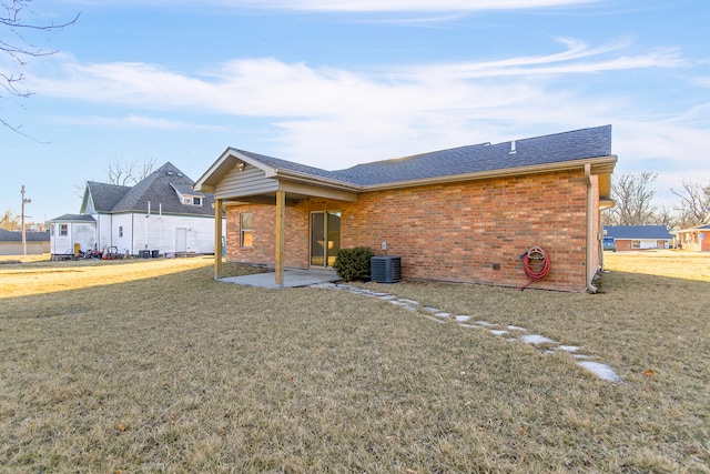 rear view of house with a shingled roof, a patio, a yard, central air condition unit, and brick siding