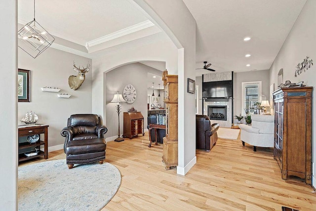 living area with a large fireplace, arched walkways, baseboards, light wood-style flooring, and recessed lighting