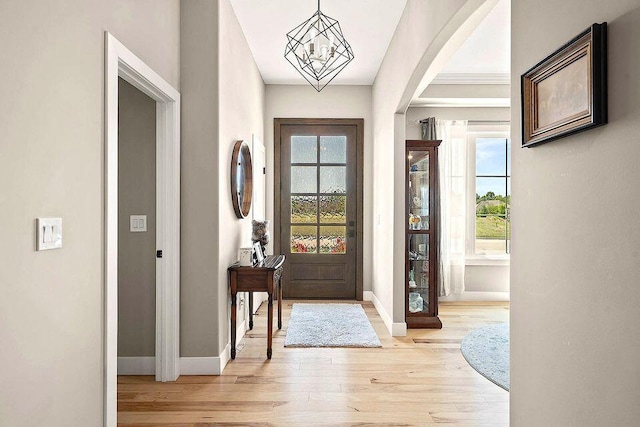 foyer featuring light wood-style floors, arched walkways, a notable chandelier, and baseboards