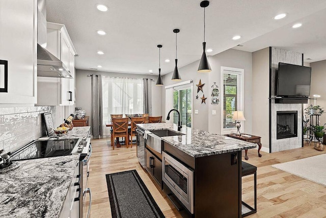 kitchen featuring a fireplace, appliances with stainless steel finishes, white cabinetry, a sink, and a kitchen bar