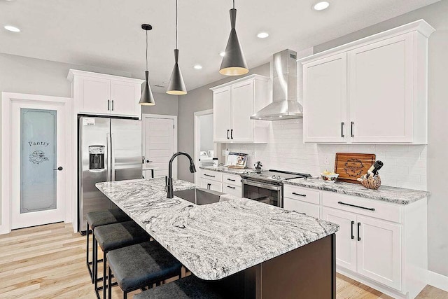 kitchen with tasteful backsplash, wall chimney exhaust hood, stainless steel appliances, a kitchen bar, and a sink