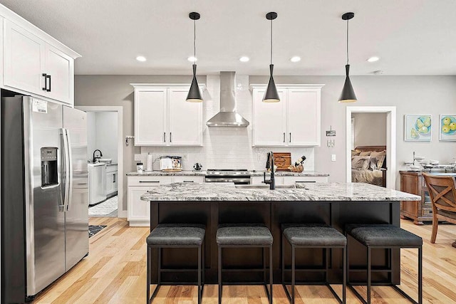 kitchen featuring appliances with stainless steel finishes, white cabinetry, a sink, and wall chimney range hood