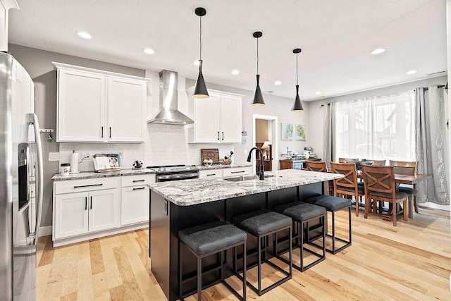 kitchen with appliances with stainless steel finishes, white cabinets, a sink, wall chimney range hood, and light wood-type flooring