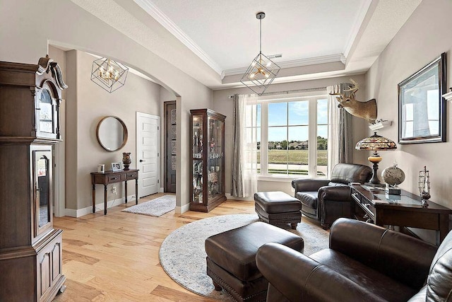 interior space featuring arched walkways, baseboards, a raised ceiling, light wood-style flooring, and crown molding