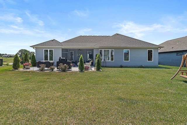 rear view of property with a shingled roof, a patio area, and a lawn