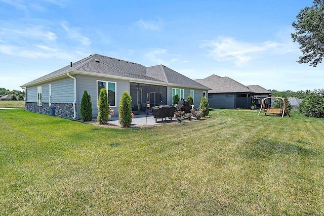 back of house featuring a playground, a yard, stone siding, roof with shingles, and a patio area