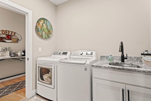 laundry area with cabinet space, light wood finished floors, baseboards, washer and clothes dryer, and a sink