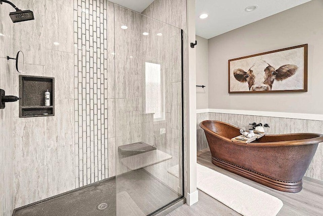 bathroom with a freestanding tub, wainscoting, a tile shower, and tile walls