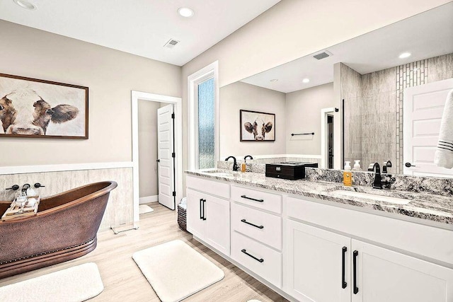 full bath with double vanity, visible vents, a sink, and wood finished floors