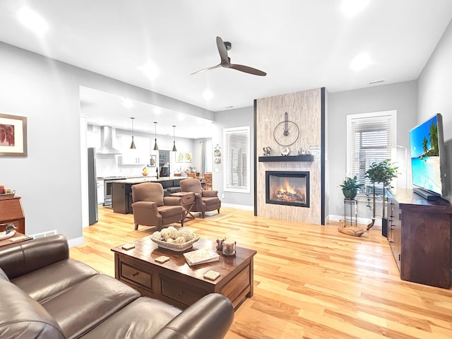 living room featuring a large fireplace, light wood-style flooring, baseboards, and a ceiling fan